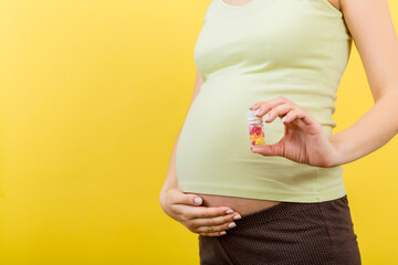 Close up of pregnant woman holding a bottle of pills against her belly at colorful background with...