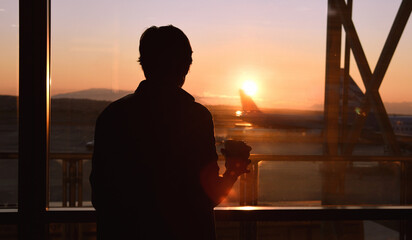 Against the backdrop of sunset and aircraft, a person drinking coffee and waiting for a flight