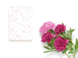 Flower composition. A bouquet of red and pink peonies and a piece of paper with a marble pattern are on a white background. Flat lay. Copy space.