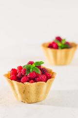 Homemade shortcrust raspberry pastry. Summer berries mini tartlets with vanilla custard and mint leaves. Fresh desserts on the white background isolated. Free copy space.