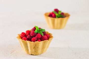 Homemade shortcrust raspberry pastry. Summer berries mini tartlets with vanilla custard and mint leaves. Fresh desserts on the white background isolated. Free copy space.