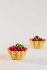 Homemade shortcrust raspberry pastry. Summer berries mini tartlets with vanilla custard and mint leaves. Fresh desserts on the white background isolated. Free copy space.