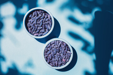 Honeysuckle berries in a blue bowl on a blue background. Shadows. Harvest