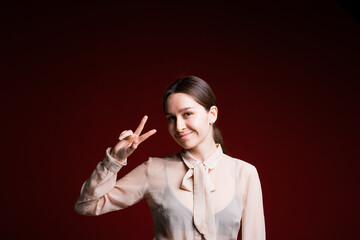 Fototapeta premium Portrait of a business girl who smiles cheerfully and shows a victory sign with her fingers on a red background