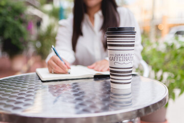 woman having coffee in café taking notes in an outdoor table having a meeting 
