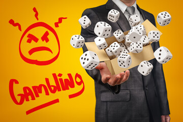Businessman holding cardboard box filled with white casino dice and 'Gambling' sign on yellow background
