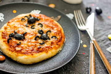 Halloween pizza with olive spiders. Halloween pizza on a plate on a dark background, next to the cutlery. How to Decorate Halloween Pizza, Scary Food