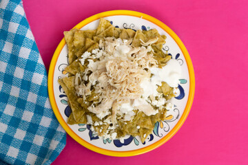 Mexican green chilaquiles with chicken and cheese on pink background