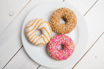 Sweet donuts, cakes on a white plate and a wooden table