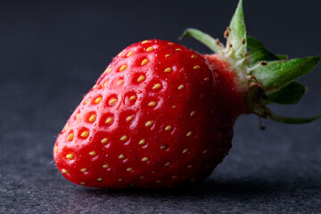 one red strawberry fruit with fine splashes on dark grey background with green leaves, side view leaning to the right, fresh and cool wet look