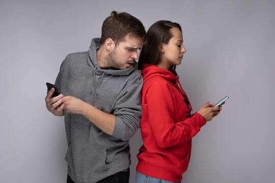 Young couple using smartphones at home. Jealous boyfriend spying his girlfriend's phone.