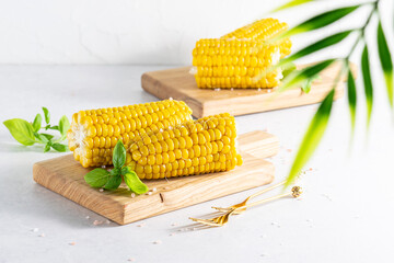 Sweet boiled corn cobs with sea salt and basil leaves on white marble table close up. Healthy diet food concept.