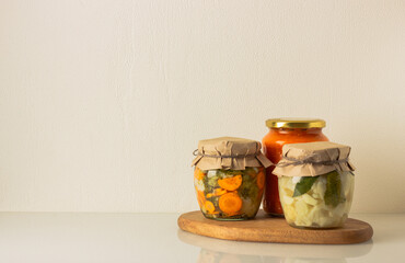 Canned homemade vegetables in a jars on wooden board: cauliflower, broccoli, carrot and zucchini in tomato sauce. Front view, copy space.