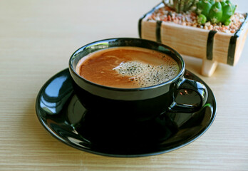 Closeup a cup of frothy hot coffee with blurry potted plant on wooden table 
