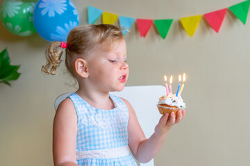 Blonde, Caucasian little girl smiling while looking at a festive cake with candles. The concept of birthday and making wishes.