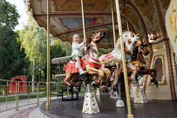 Little girl rides a carousel in an amusement park