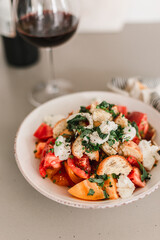 Tomato crostini salad with mozzarella cheese. Refreshing healthy dinner. Glass of red wine. Nourishing salad lunch. Panzanella heirloom tomato summer seasonal Italian salad. Colorful plate.