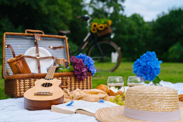 Summer picnic on sunny day with bread, fruit, bouquet hydrangea flowers, glasses wine, straw hat,...