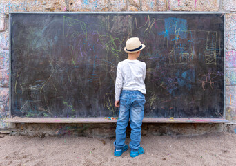 cute little boy writing something with chalk on blackboard