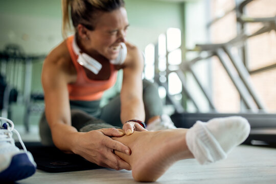 Close-up of female athlete feeling pain in her ankle during sports training at health club.