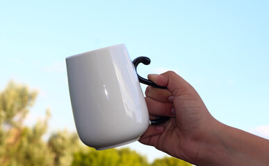 White mug in the hand of a man against the background of nature.