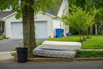 Two old worn out mattresses by a tree at the curb near a trash can in front of a house © ALAN