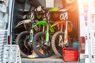 Three bright dirty sport motocross motorcycles stand in tail of technical support assistance van in...