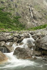 Water flows over rocks at the bottom of a mountain waterfall. Beautiful mountain river. Vertical photo