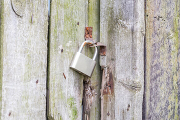 Old padlock on the aged rotten wooden abandoned gate. Close up view.
