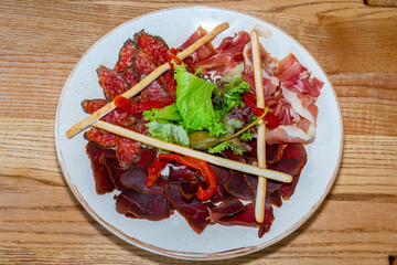 Trio of dried delicacies. Basturma, prosciutto, sausage flat. Plate with delicacies