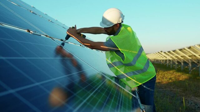 Slow motion man worker fixing solar panel to a metal basis with a drill in a sunny day green environmental rooftop construction engineer photovoltaic electricity battery utility close up