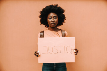 Attractive serious african woman standing and holding paper with JUSTICE title.