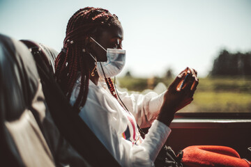 Side view of a young African woman in a virus protection mask, with braids and with a smartphone in...
