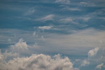 white cumulus clouds dissolving in the foreground and in the background white cirrus clouds blown by the winds under a blue sky.
