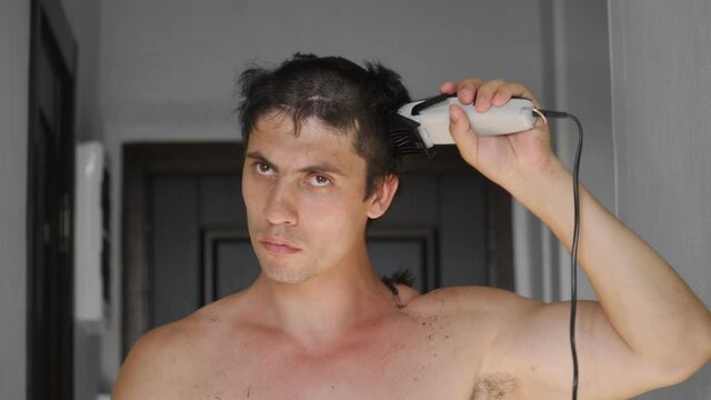 A man cuts himself with an electric hair clipper at home. Maintaining social distance. Epidemic of coronavirus infection covid-19