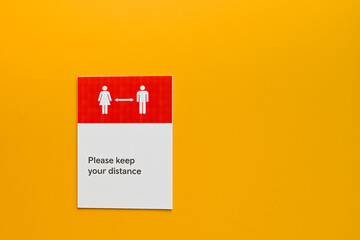 Notice on a plain yellow wall asking people to maintain social distancing. No people. Copy space.