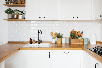 View on white kitchen in scandinavian style, kitchen details, plants on wooden table