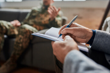 Notes. Close up of hands of psychologist making notes while communicating with military man during...