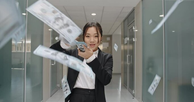 Successful asian manager in formal suit standing in office hall, throwing money in the air, celebrating her victory- way to success concept 4k