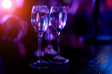 two small glasses on a long leg on a wooden table in the night light with a drink 