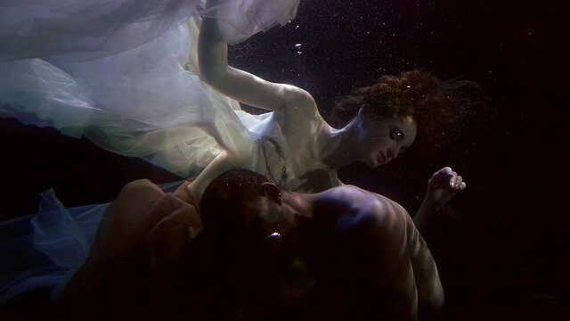 multiracial lovers underwater, man and woman are swimming inside dark deepness
