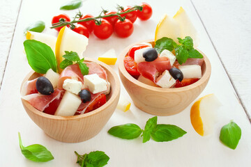 Salad with Parma ham, melon, cherry tomatoes, feta cheese and olives, decorated with mint and basil leaves