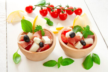 Salad with Parma ham, melon, cherry tomatoes, feta cheese and olives, decorated with mint and basil...