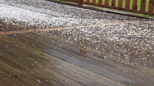 Wet wooden terrace after strong summer hail storm covered by white round frozen small hailstones. Hot sunny summer weather gets unpredictable weather conditions. Original sound included