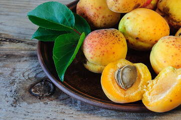 Ripe apricots with green leaves on a ceramic plate on a wooden table
