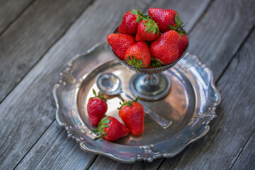 Ripe strawberries in silverware on old wooden background