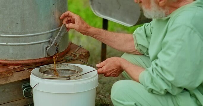 Beekeeper turns the honey extractor handle and a stream of fresh honey pours out. Honey pumping process, natural eco-product. 4k, 10bit, ProRes
