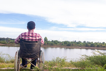 Obraz premium Young disabled man with river background.He is sitting on wheelchair and looking into river.