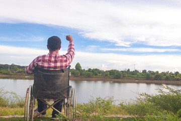 Obraz premium Young disabled man with river background.He is sitting on wheelchair and looking into river.