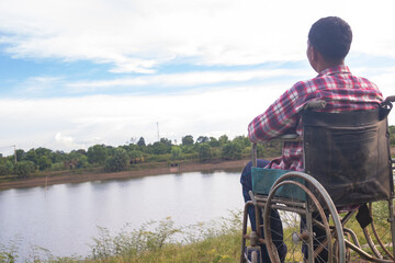 Naklejka premium Young disabled man with river background.He is sitting on wheelchair and looking into river.